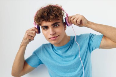 Mavi tişörtlü yakışıklı genç adam. Pembe kulaklıklar. İzole edilmiş arka plan.