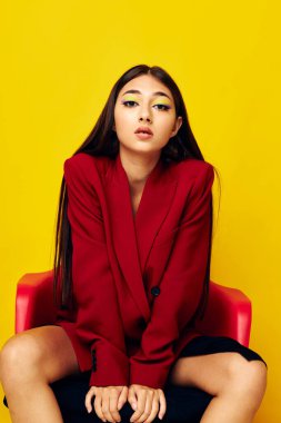 Kırmızı ceketli güzel esmer, sarı arka planda oturuyor.