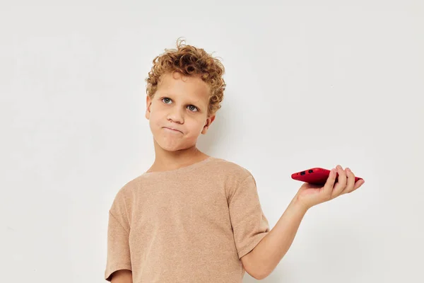 Mignon garçon avec les cheveux bouclés tenant un fond de lumière téléphone rouge — Photo