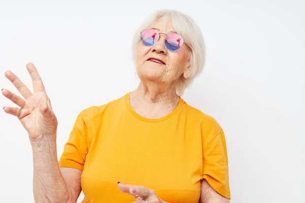 Portrait of an old friendly woman in casual t-shirt sunglasses light background