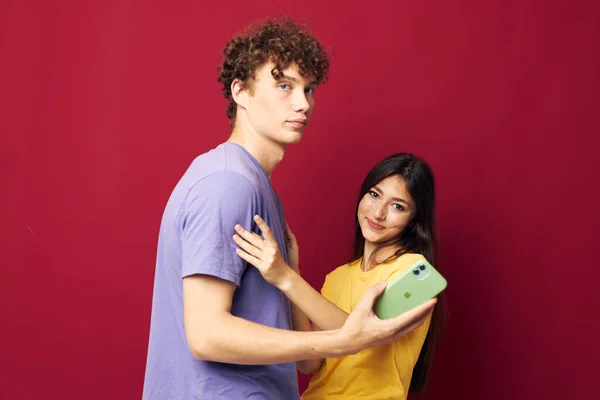 Agradable chico y chica en coloridas camisetas con un fondo rojo teléfono — Foto de Stock
