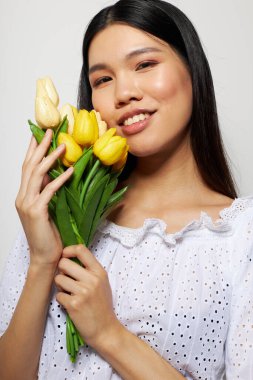 Beyaz gömlekli güzel bir Asyalı kadın. Çiçekler bahar. Stüdyo modeli gibi poz veriyor.