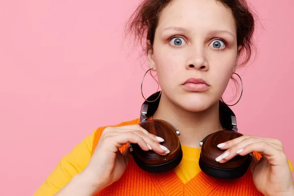 Belle femme dans un pull orange écouteurs musique divertissement fond rose inchangé — Photo