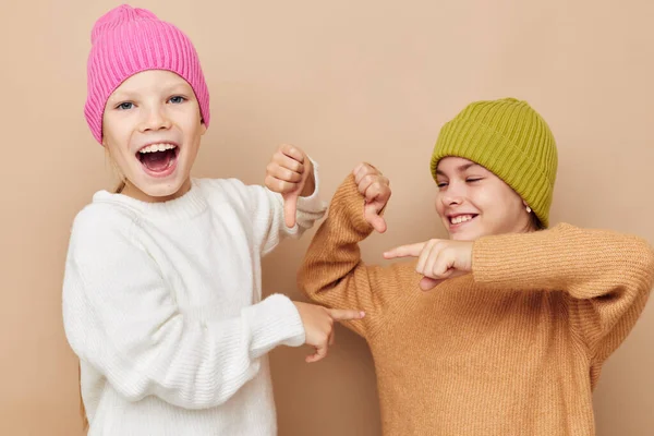 Twee kleine meisjes in truien en hoeden knuffel vriendschap beige achtergrond — Stockfoto