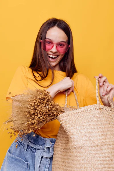 Genç kadın hasır çanta elinde pembe gözlük sarı arka plan