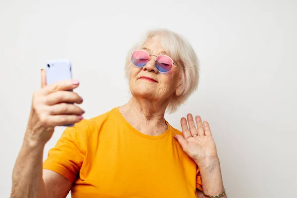 黄色のTシャツを着た引退したおばあちゃんの写真は、電話のクローズアップ感情によるコミュニケーションをポーズ — ストック写真
