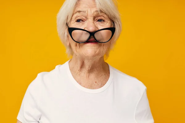 Smiling elderly woman in a white t-shirt wears glasses isolated background — Stock Photo, Image