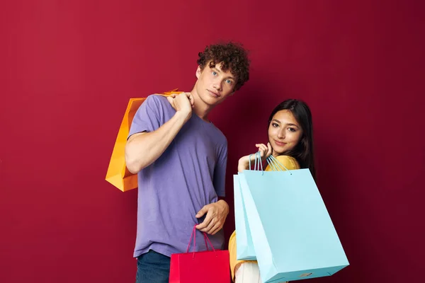 Portrait of a man and a woman in colorful T-shirts with bags Shopping red background unaltered — Stockfoto