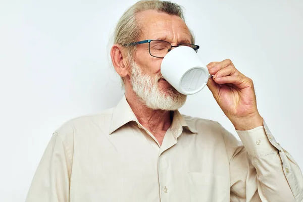 Starší muž pije z hrnku na bílém pozadí a usmívá — Stock fotografie