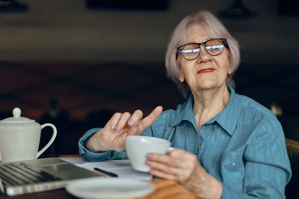 Retrato de una anciana con gafas sentada en una mesa frente a un portátil Freelancer trabaja sin alteraciones — Foto de Stock
