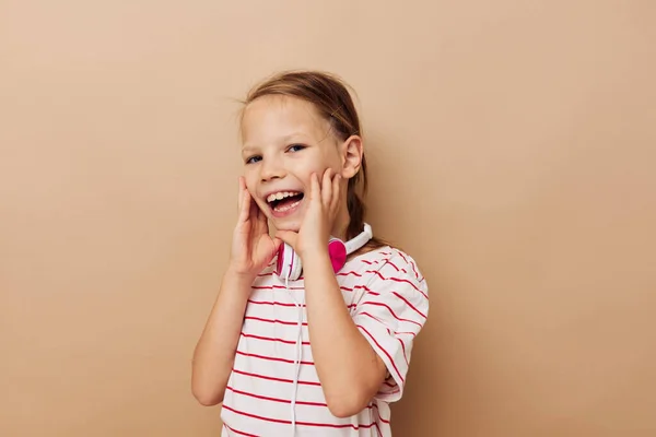Çizgili tişörtlü kulaklıklı küçük kız çocukluğunu değiştirmeden el kol hareketi yapar. — Stok fotoğraf