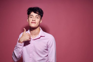 Pembe gömlekli hoş bir adam elleri pembe arka planda el kol hareketi yapıyor.