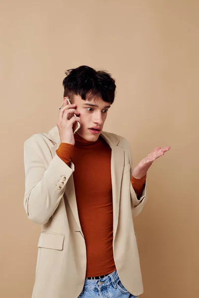 Retrato de un joven con una chaqueta beige hablando sobre el fondo de la luz del teléfono inalterado — Foto de Stock