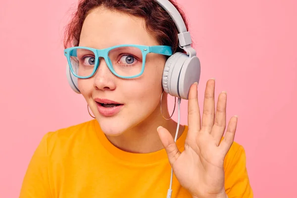 Chica divertida con gafas azules escuchando música en los auriculares de fondo rosa inalterado — Foto de Stock