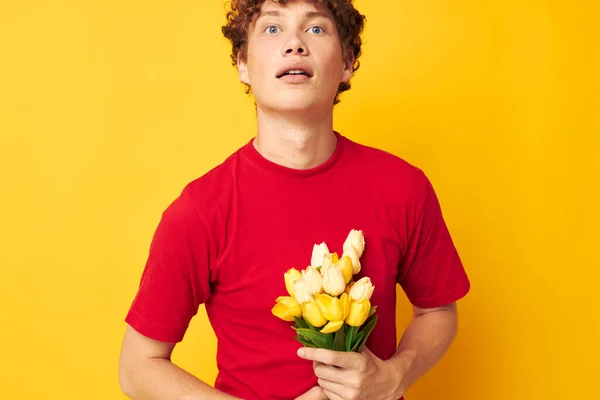 Retrato de un joven rizado romántico posando con un ramo amarillo de flores fondo amarillo inalterado — Foto de Stock