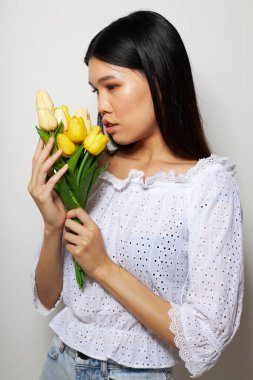 Beyaz gömlekli güzel bir Asyalı kadın portresi. Çiçekler. Arka planda hafif bir poz veriyor.