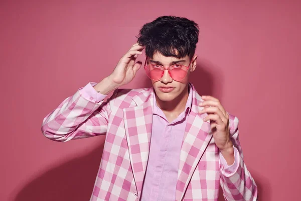 Un hombre joven chaqueta a cuadros gafas de color rosa moda estilo moderno rosa fondo inalterado — Foto de Stock