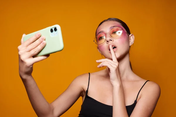 Portrait of beautiful young woman looks at the phone bright makeup posing fashion emotions yellow background unaltered — Foto Stock