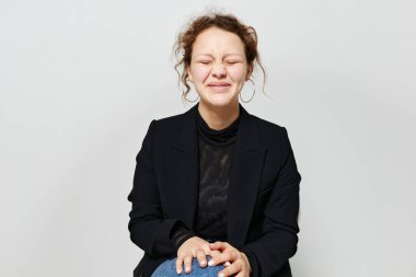 Siyah ceketli bir sandalyede oturan neşeli bir kadın. Arka planda hafif bir poz veriyor.