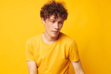Sarı tişört giyen genç bir kıvırcık adamın portresi değiştirilmemiş sarı arka plan pozu veriyor.