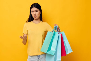 Sarı tişörtlü, Asyalı bir kadın. Çok renkli alışveriş çantalı. Stüdyo modeli değiştirilmemiş.