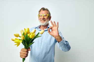 Mavi gömlekli yaşlı bir adam ve buket çiçekli bir manzara.