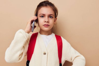 Sırt çantasıyla telefonda konuşan mutlu gülümseyen kız çocuğunun portresi.