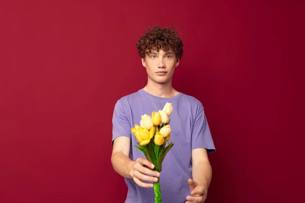 Έφηβος κρατώντας ένα κίτρινο μπουκέτο λουλούδια μωβ t-shirts κόκκινο φόντο αμετάβλητη — Φωτογραφία Αρχείου