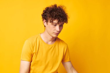 Genç kıvırcık saçlı adam, gençlik tarzı gözlük stüdyosu gündelik kıyafetleri, sarı arka plan değiştirilmemiş.