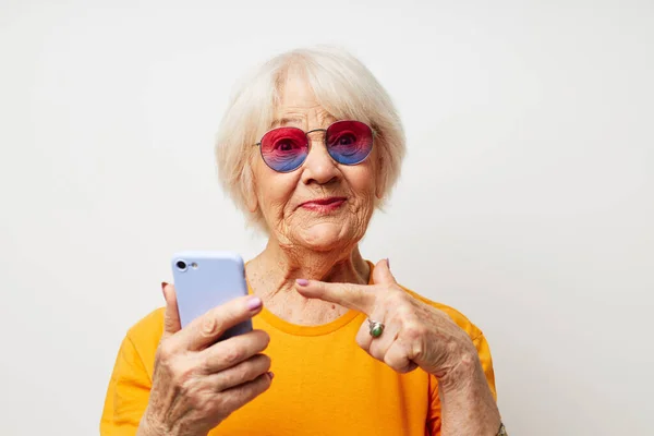 손전등으로 스마트폰을 들고 유행하는 안경을 쓰고 웃고 있는 노부인 — 스톡 사진