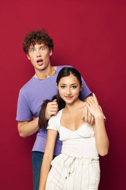 Bir adam bir kızın arkasında durur ve saçlarını kırmızı arka planda tutar.