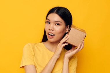Elinde küçük bir kutu hediye taşıyan kadın. Sarı arka plan.