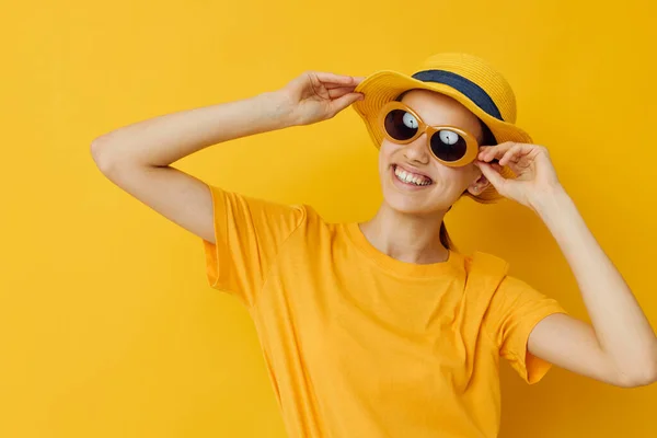 戴着太阳镜的漂亮姑娘，黄色T恤，帽子夏天的黄色背景 — 图库照片