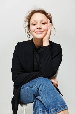 Siyah ceketli bir sandalyede oturan neşeli kadın yaşam tarzını değiştirmeden poz veriyor.