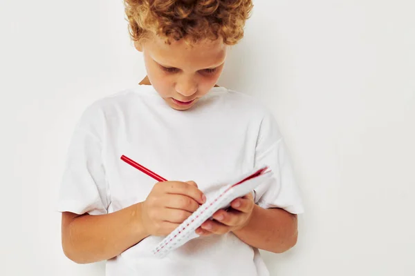 Веселый мальчик с вьющимися волосами рисует блокнот карандашом — стоковое фото