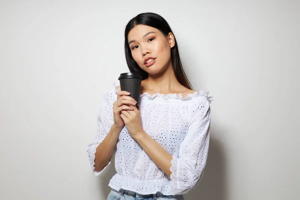 Encantadora jovem mulher asiática um copo preto nas mãos de uma bebida como um sorriso isolado fundo inalterado — Fotografia de Stock