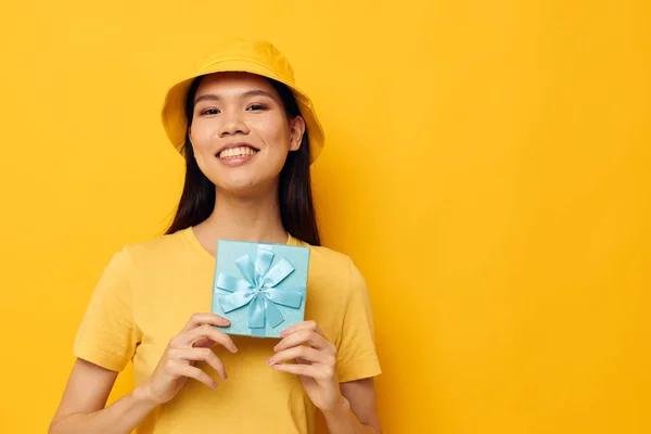 Charming young Asian woman in a yellow T-shirt and a hat with a gift yellow background unaltered — Stock Photo, Image