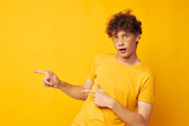 Genç kıvırcık saçlı adam sarı t-shirt gözlükleri moda el hareketleri tek renkli fotoğraf