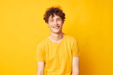 Şık sarı tişört giyen genç bir kıvırcık adamın portresi tek renkli poz veriyor.