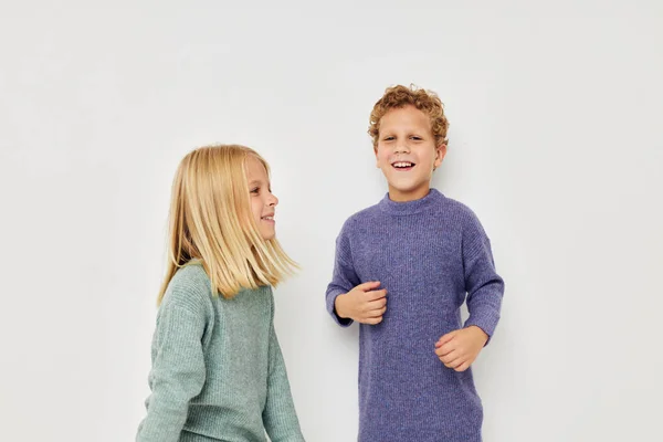 Little boy and girl in multi-colored sweaters posing for fun light background — Foto Stock