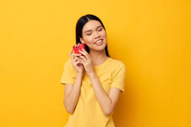 Elinde hediye kutusu olan bir kadın sarı arka plan pozu veriyor.