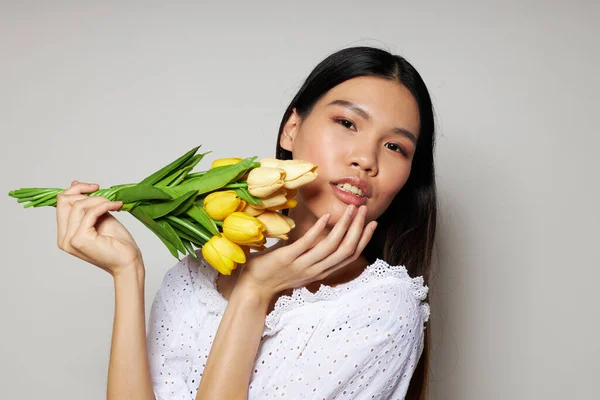 Портретна азіатська вродлива молода жінка з букетом квітів посміхається зблизька освітленим фоном незмінним — стокове фото