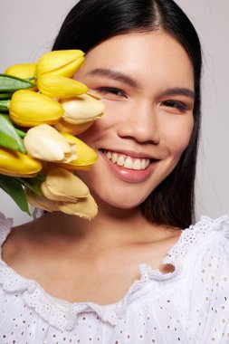 Bir buket çiçekle güzel bir esmer. Gülümse. Kapalı bir arka plan, değiştirilmemiş.