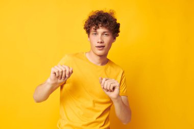 Genç, kıvırcık saçlı, sarı tişörtlü, el hareketleriyle izole edilmiş arka planı değiştirilmemiş.