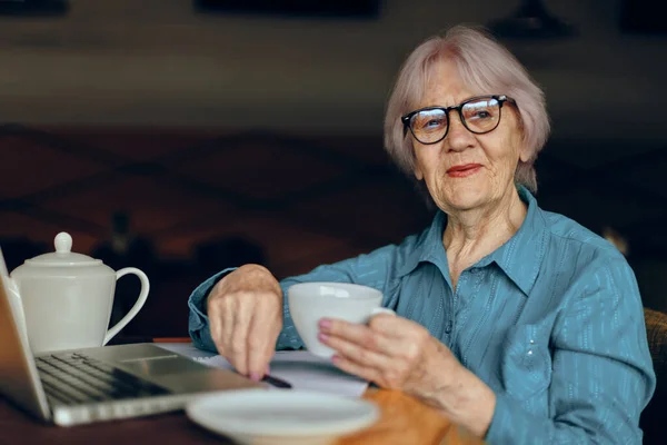 Portrait d'une femme âgée avec des lunettes assise à une table devant un ordinateur portable — Photo