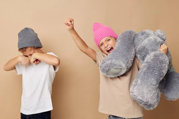 Photo of two children in multi-colored hats entertainment posing beige background — 图库照片