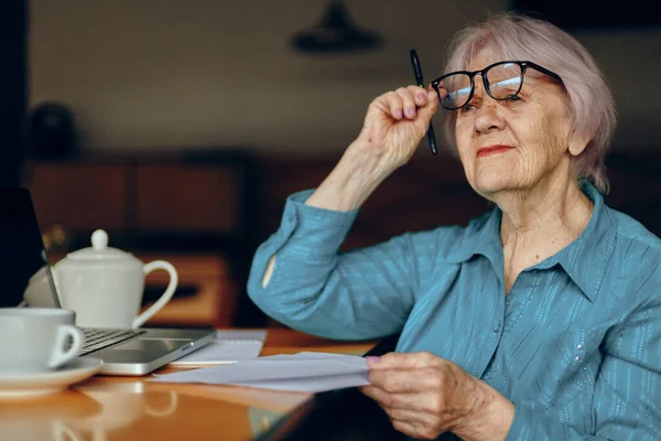 Retrato de una anciana con gafas sentada en una mesa frente a un portátil Estilo de vida inalterado — Foto de Stock