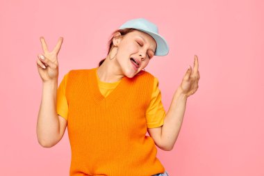 Mavi şapkalı turuncu kazaklı komik kız el hareketleriyle yaşam tarzını değiştirmemiş.