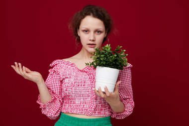 Yeşil şortlu çekici genç bir kadın çiçek saksısı, değişmeden yakın plan poz veriyor.