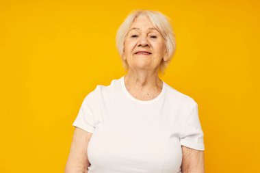 Gülümseyen yaşlı bir kadın tişört giyer ve elleriyle duygularını kapatır.